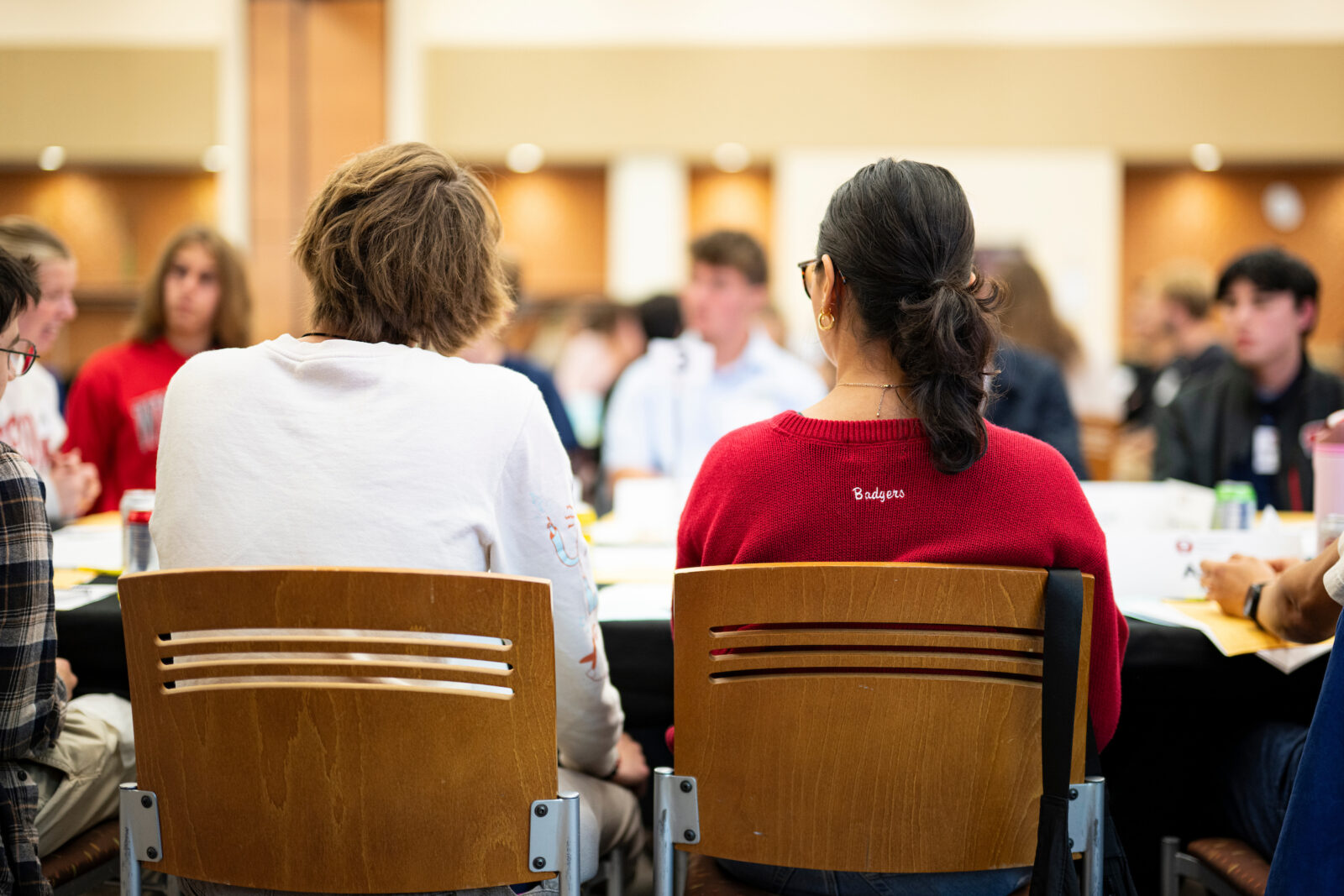 Two people with sitting with their backs facing the camera at a large group at a table